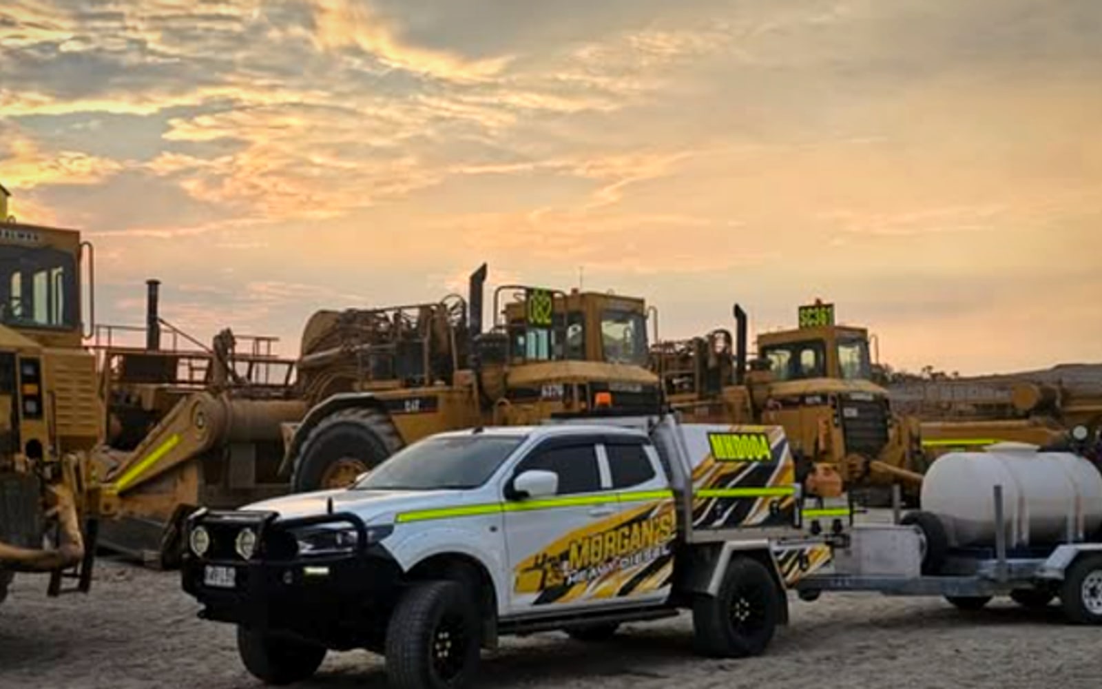 Morgan's Heavy Diesel service ute parked beside a fleet of earthmoving machinery at dusk